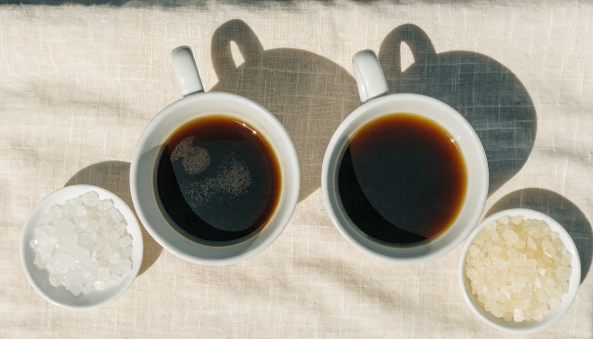 Vista cenital de dos tazas de café con eritritol y xilitol en cuencos blancos sobre lino crema
